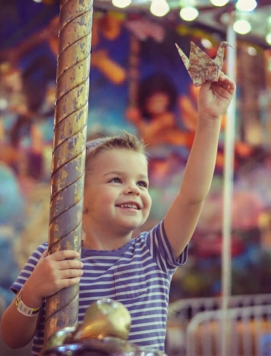 A boy on a carousel ride holding an origami crane